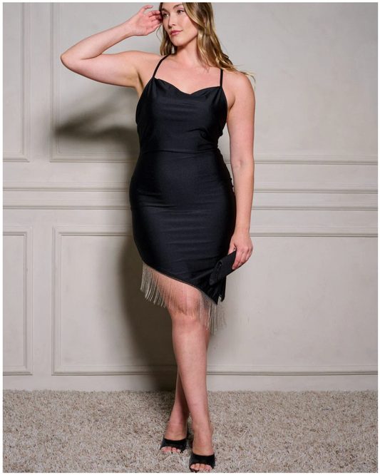 Woman wearing a black satin dress with fringe details against a neutral wall.