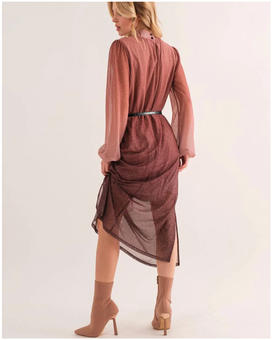 Woman wearing a long, sheer brown dress with a belt and high-heeled shoes on a white background